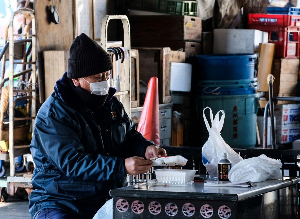 Man in winter attire eating at an indoor warehouse. Scene depicts an urban lifestyle moment.